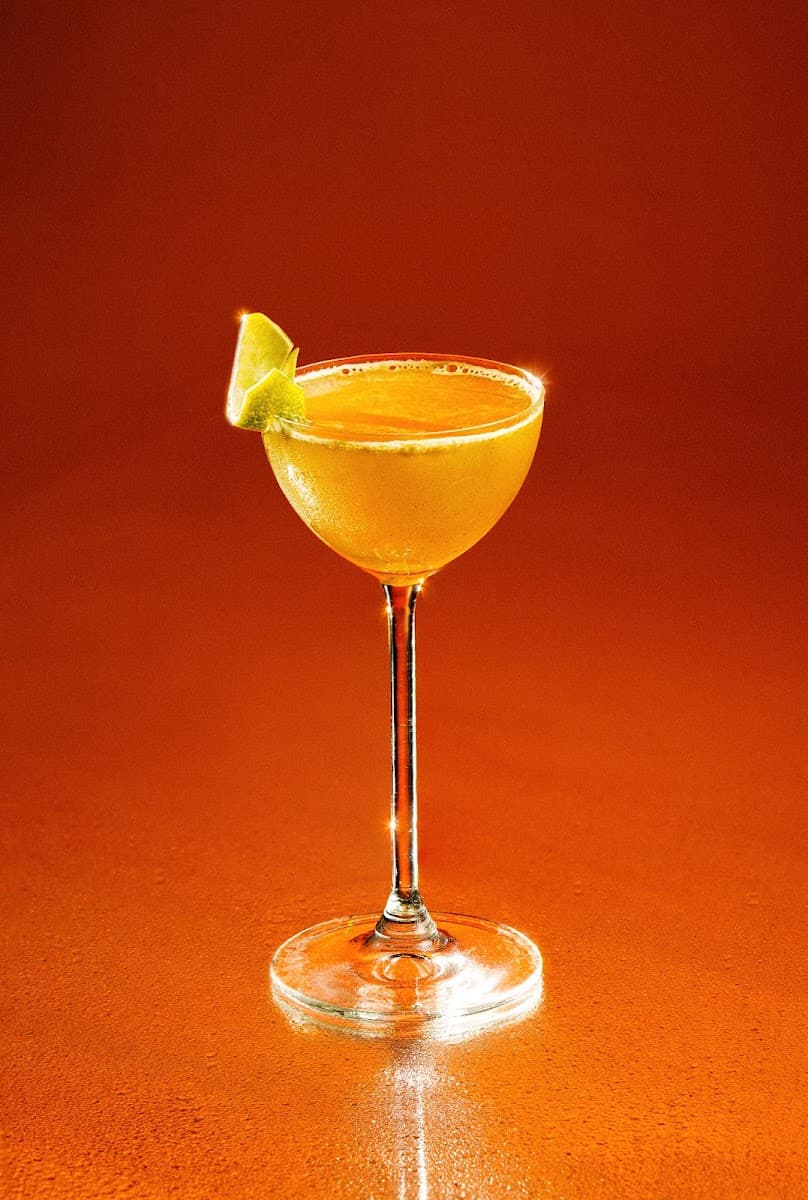 Cocktail galben cu felie de lime, pe fundal portocaliu